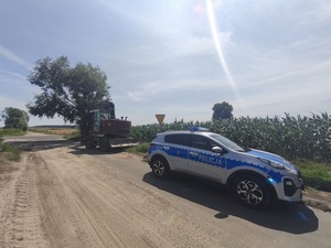 koparka i radiowóz stoją przy drodze obok pola z kukurydzą