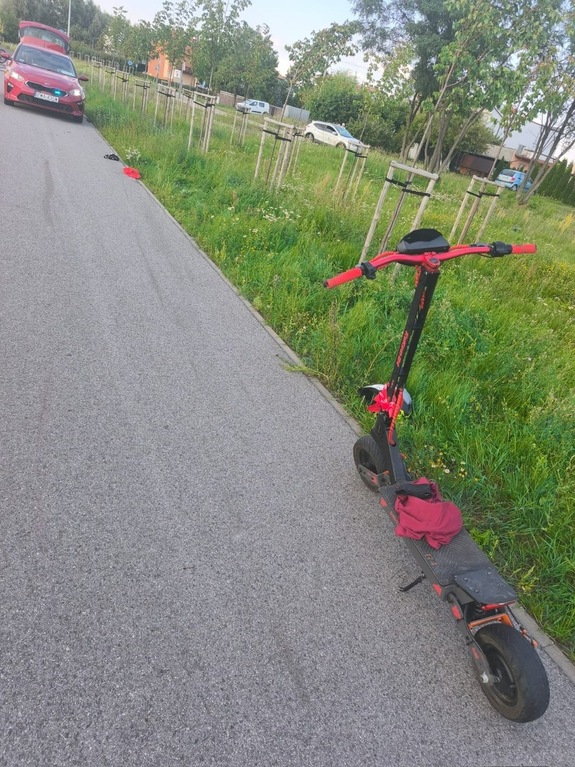hulajnoga stoi przy drodze pieszo-rowerowej, w oddali stoi radiowóz